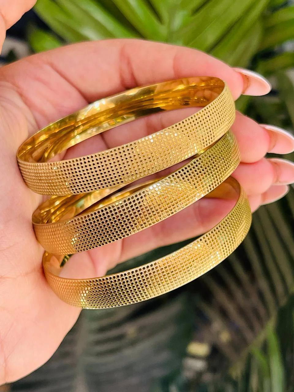 طقم مكون من ثلاثة أساور ذهبية بنقشة ليزر محببة ولامعة على يد امرأة