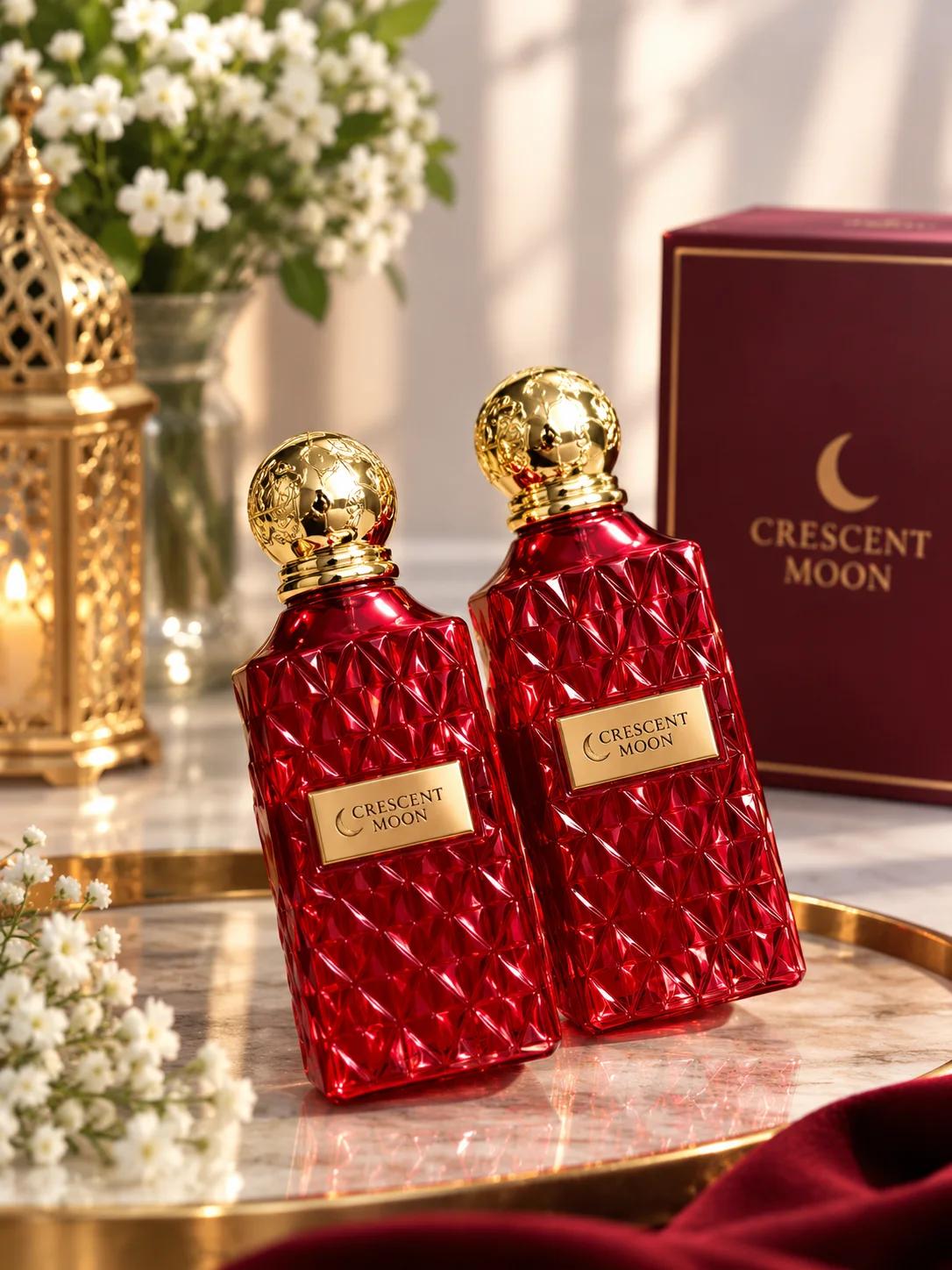 زجاجتان من عطر كريسنت مون الأحمر الفاخر بغطاء ذهبي كروي بجانب العلبة العنابية الأنيقة